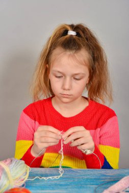 Çizgili kazaklı kız ciddi bir yüzle örgü örmeyi öğreniyor..