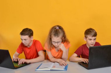 Çocuklar evde eğitim görüyor, iki erkek bir dizüstü bilgisayar başında oturuyor, bir kız kitap okuyor. Ev kavramında çevrimiçi öğrenim.
