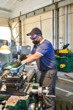 Koruyucu bir antiviral maske takan çalışan bir döner torna tezgahında metal kesiyor.