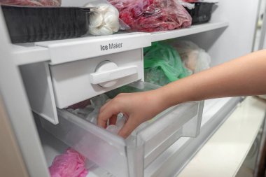 The girl takes ice from the ice maker of the freezer for cooling drinks. clipart