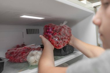 A woman puts frozen fruit products in the freezer, for long-term preservation. clipart