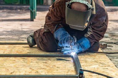 Elektrikli kaynakçı, bir elektrot ile kaynak yaparak şekilli bir borudan metal bir yapı oluşturur..