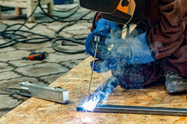 Elektrikli kaynakçı, bir elektrot ile kaynak yaparak şekilli bir borudan metal bir yapı oluşturur..