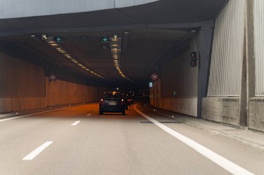 Araçlar, yukarıdaki ışıklar ve trafik ışıklarıyla aydınlatılan loş bir şehir tünelinde yol alırlar. Yol pürüzsüz bariyerlerle kaplı, akşam koşuşturması arasında organize bir akış yaratıyor..