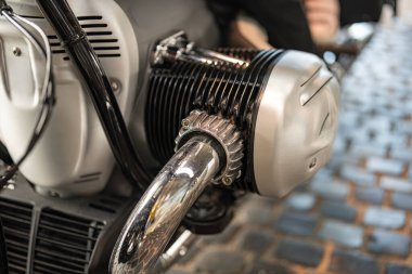 Klasik bir motosiklet motoru, krom detaylar ve karmaşık bileşenlerle sergilenir. Sahne bir kaldırım taşı caddesi, güneşli bir öğleden sonra havası yakalıyor..