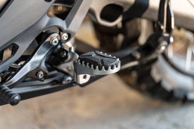 Motosikletli ayak mandalının mekanik özelliklerinin detaylı görüntüsü. Çekim, metal parçalarının dokusunu ve parıltısını iyi aydınlatılmış bir garajda yakalıyor..