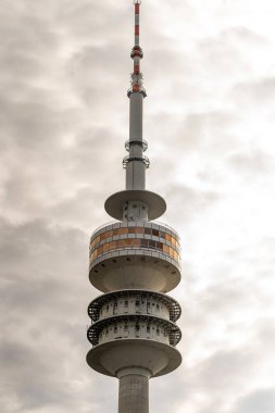 Uzun bir telekomünikasyon kulesi, öğleden sonra saatlerinde karanlık ve kasvetli bulutların altında belirgin bir şekilde duruyor. Yapısı eşsiz tasarımı ve rengi ile dikkat çekicidir..