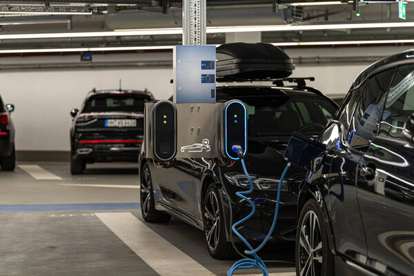 Электрические транспортные средства припаркованы в хорошо освещенном подземном гараже, в то время как один автомобиль подключен к зарядной станции. Установка способствует устойчивому транспорту.