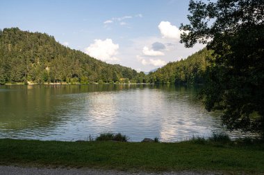 Sakin sular, kabarık bulutlar gökyüzünde süzülürken etrafındaki tepelerin yeşilliğini yansıtır. Rahatlamak ve öğleden sonra doğanın güzelliğinin tadını çıkarmak için mükemmel bir yer..