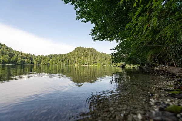 Güneşli bir günde gölün sakin suları çevredeki tepeleri ve ağaçları yansıtır. Doğanın el değmemiş güzelliğinde barışçıl bir atmosfer yaratır..