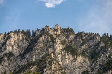 Parlak mavi gökyüzüne karşı yükselen granit kayalıklar. Engebeli arazi ağaçlarla süslenerek gün ışığında kayalık yüzeyle canlı bir kontrast oluşturuyor..