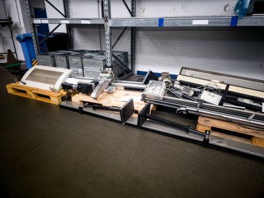 Endüstriyel makine parçaları bir depodaki ahşap paletlere yerleştirildi. Dekor iyi aydınlatılmış, temiz zeminde dinlenen çeşitli bileşenleri gösteriyor..