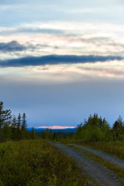 Turuncu parlaklık ve katmanlı bulutlar, Granbergsliden yakınlarındaki bir yoldan görüldü, İsveç