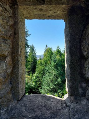 Taş pencere, orman ağaçlarının ve mavi gökyüzünün altındaki uzak tepelerin çerçevesini açıyor..