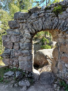Ormanın doğal ortamında kayalar ve bitki örtüsü arasında duran taş kemer yolu yıkıntısı..