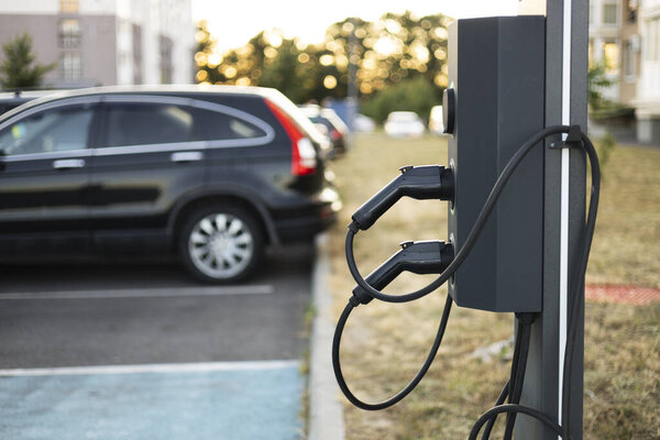 Современная электростанция зарядки транспортных средств с автомобилем, припаркованным на заднем плане. Чистый состав с пространством для текста, идеально подходит для экологического транспорта, зеленой энергии и устойчивого развития темы.