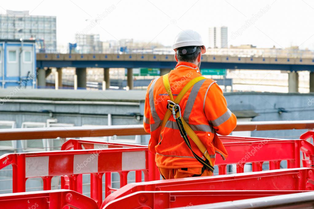 Back view of a construction worker walking into a building site in Canary Wharf, London