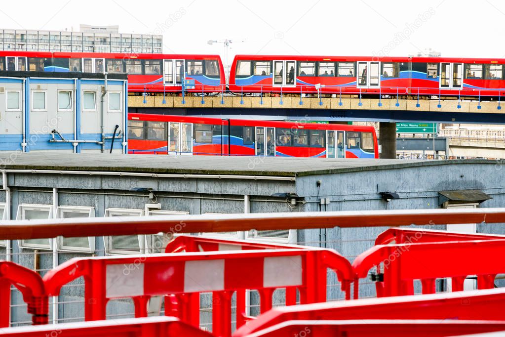 Two light trains crossing each other, seen through a construction site in Canary Wharf, London