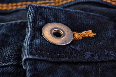 Denim kot desenli yırtık. Renkli pamuk kumaşın dokusu. Dikilmiş desenli kot pantolon. Moda pantolonu düğmesi. Kotun üzerindeki perçin ve cep. İplik ve kumaş yapısı.