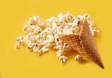 Bir gözleme koni dondurma yemeye parlak sarı bir arka plan üzerinde patlamış mısır. Film. Fast food. Mısır