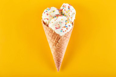 Dondurma topları renkli şeker sprinkles bir gözleme koni üzerinde sarı bir arka plan ile. Vanilyalı dondurma waffle koni.