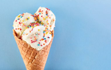 Dondurma topları renkli şeker sprinkles bir gözleme koni üzerinde mavi bir arka plan ile. Vanilyalı dondurma waffle koni.