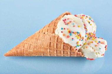 Dondurma topları renkli şeker sprinkles bir gözleme koni üzerinde mavi bir arka plan ile. Vanilyalı dondurma waffle koni.