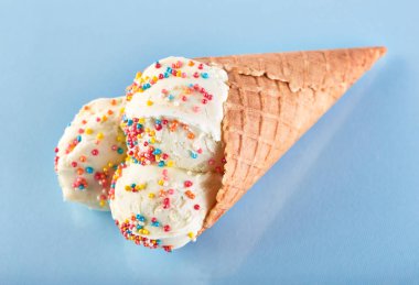 Dondurma topları renkli şeker sprinkles bir gözleme koni üzerinde mavi bir arka plan ile. Vanilyalı dondurma waffle koni.
