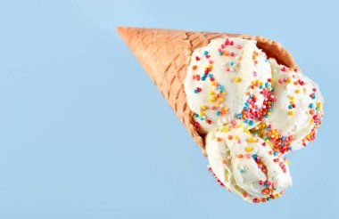 Dondurma topları renkli şeker sprinkles bir gözleme koni üzerinde mavi bir arka plan ile. Vanilyalı dondurma waffle koni.