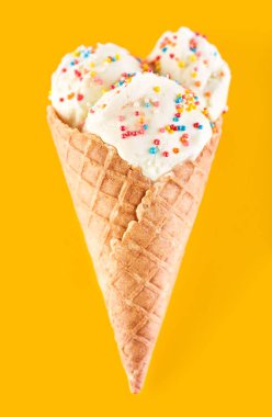 Dondurma topları renkli şeker sprinkles bir gözleme koni üzerinde sarı bir arka plan ile. Vanilyalı dondurma waffle koni.