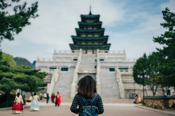 Young asian woman traveler with backpack traveling into the Gyeongbokgung Palace  with green tree in background at Seoul city, South Korea.