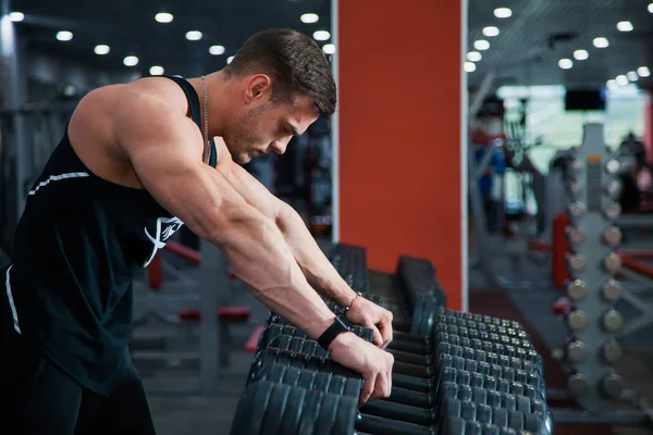 Uygun erkek atlet dumbbell egzersiz için hazırlanıyor. Fitness salonunda yakışıklı adam istirahat etmek ve nefes al. Fitness, welness ve aktif yaşam tarzı kavramı.