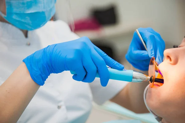 Female dentist work with light-curing seal, patient with caries on chair. Stomatologist and patient at clinical office. Toothcare concept