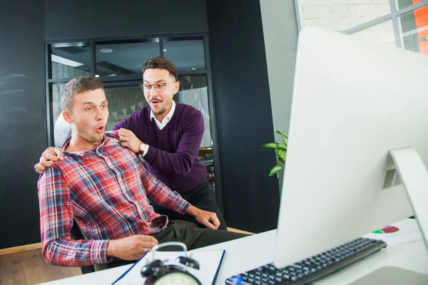 Two happy men near computer monitor, joyful moment. Business success concept