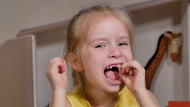 小さな女の子は 彼女の前部ゆるい歯を持っています ミルクの歯は落ちる準備ができています その子は大人になって幸せだ — ストック動画