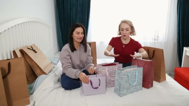 Dos mujeres atractivas se sientan en la cama y hablan de ropa nueva de compras . — Vídeo de stock