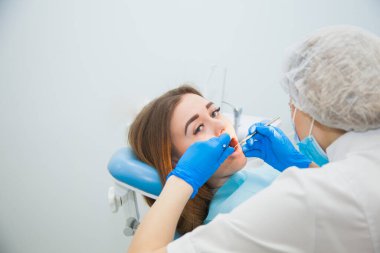 Mavi eldivenler ve koruyucu maskeyle diş dolgusunu tedavi eden kadın dişçi..