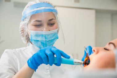 Mavi eldivenler ve koruyucu maskeyle diş dolgusunu tedavi eden kadın dişçi..