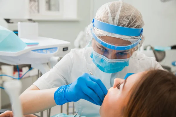 Dentystka leczy ubytek zębów w niebieskich rękawiczkach i masce ochronnej. — Zdjęcie stockowe