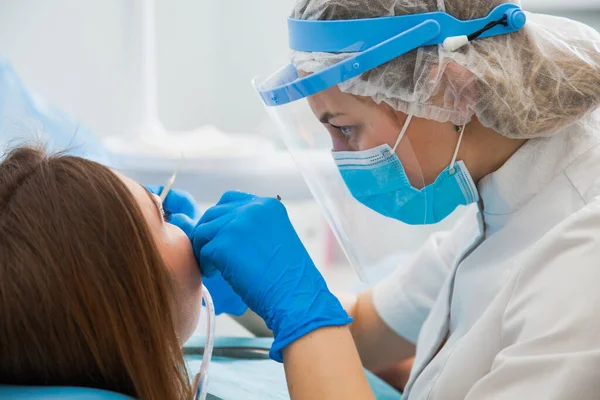 Dentystka leczy ubytek zębów w niebieskich rękawiczkach i masce ochronnej. — Zdjęcie stockowe