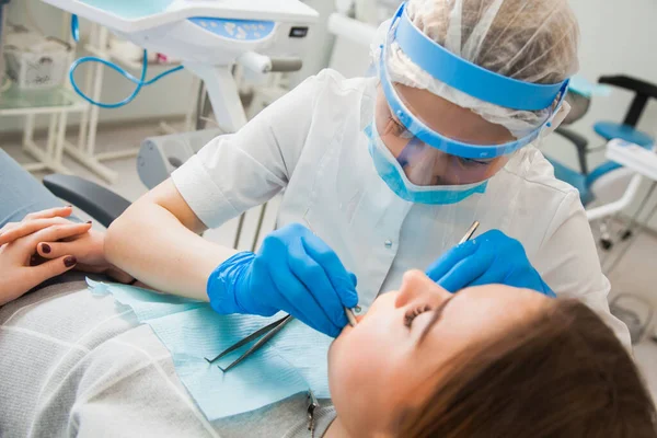 Female dentist curing teeth cavity in blue gloves and protective mask.