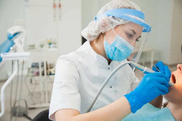 Female dentist curing teeth cavity in blue gloves and protective mask.