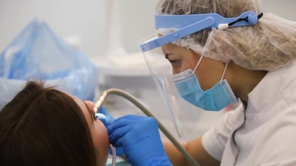 Closeup of young dentist in protective mask and glasses curing tooth cavity. — Stock Video