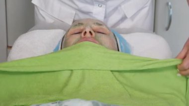 Güzellik uzmanının elleri, sıcak havlu kullanarak güzellik maskesini çıkartır.