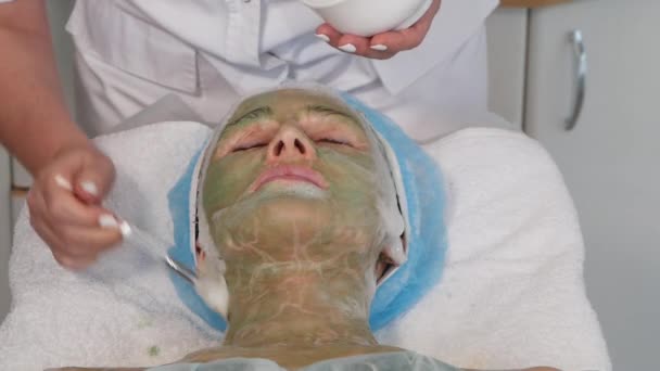 Mãos Cosmetician aplicando espuma de limpeza no rosto das mulheres com máscara verde . — Vídeo de Stock