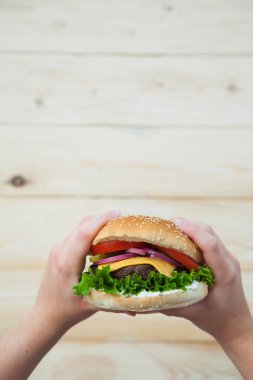 Elleri ahşap masada ev yapımı sığır burger tutuyor..