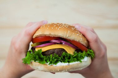 Elleri ahşap masada ev yapımı sığır burger tutuyor..