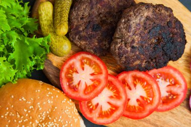 Karanlık masa üzerinde sığır burger malzemeleri seti.
