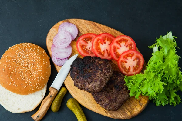 Set of beef burger ingredients on dark table.