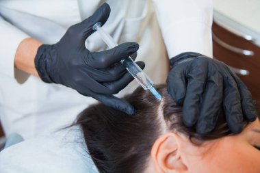 Trikoloğun muayenehanesinde tanınmayan bir kadın kafasına iğne vuruluyor..